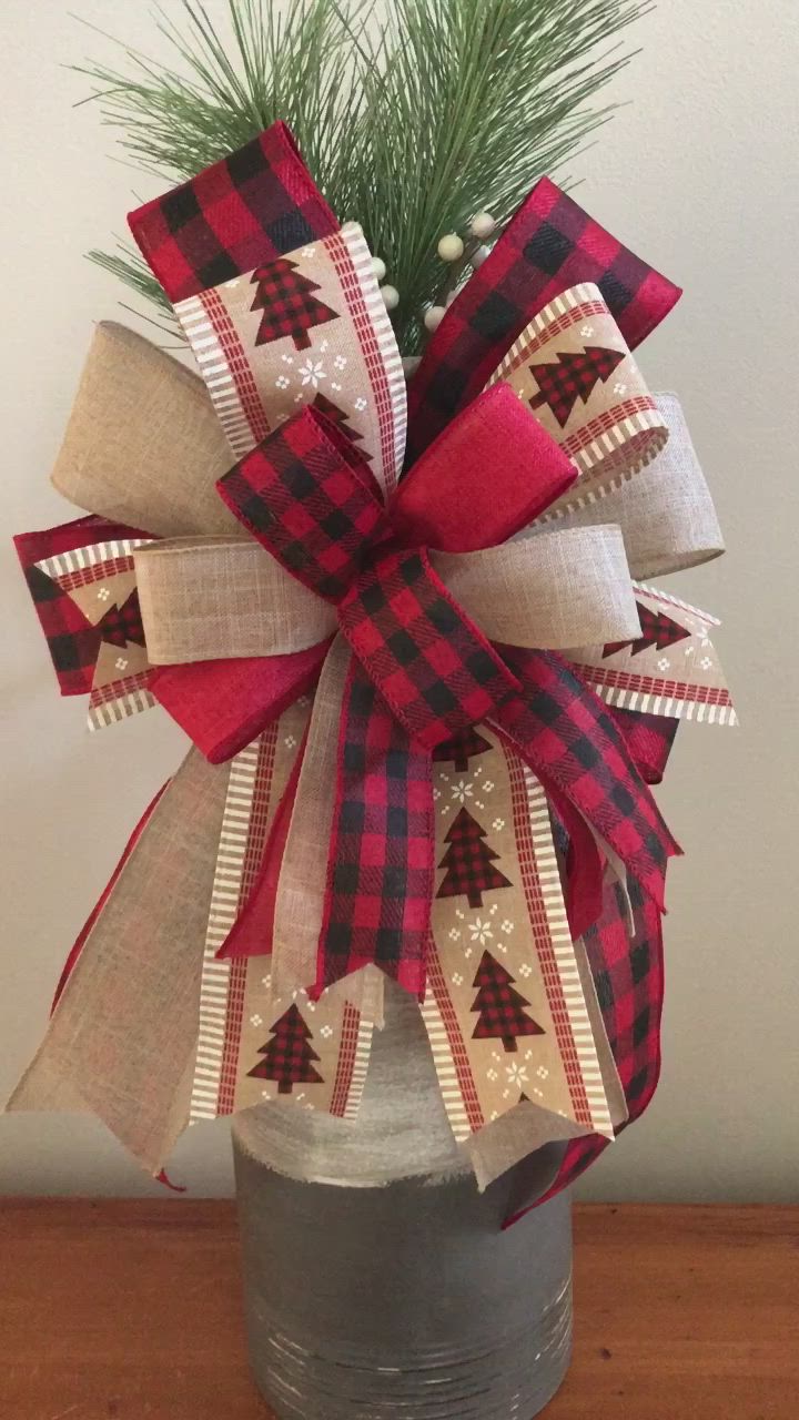 This may contain: a red and black plaid christmas bow on top of a metal can with pine branches