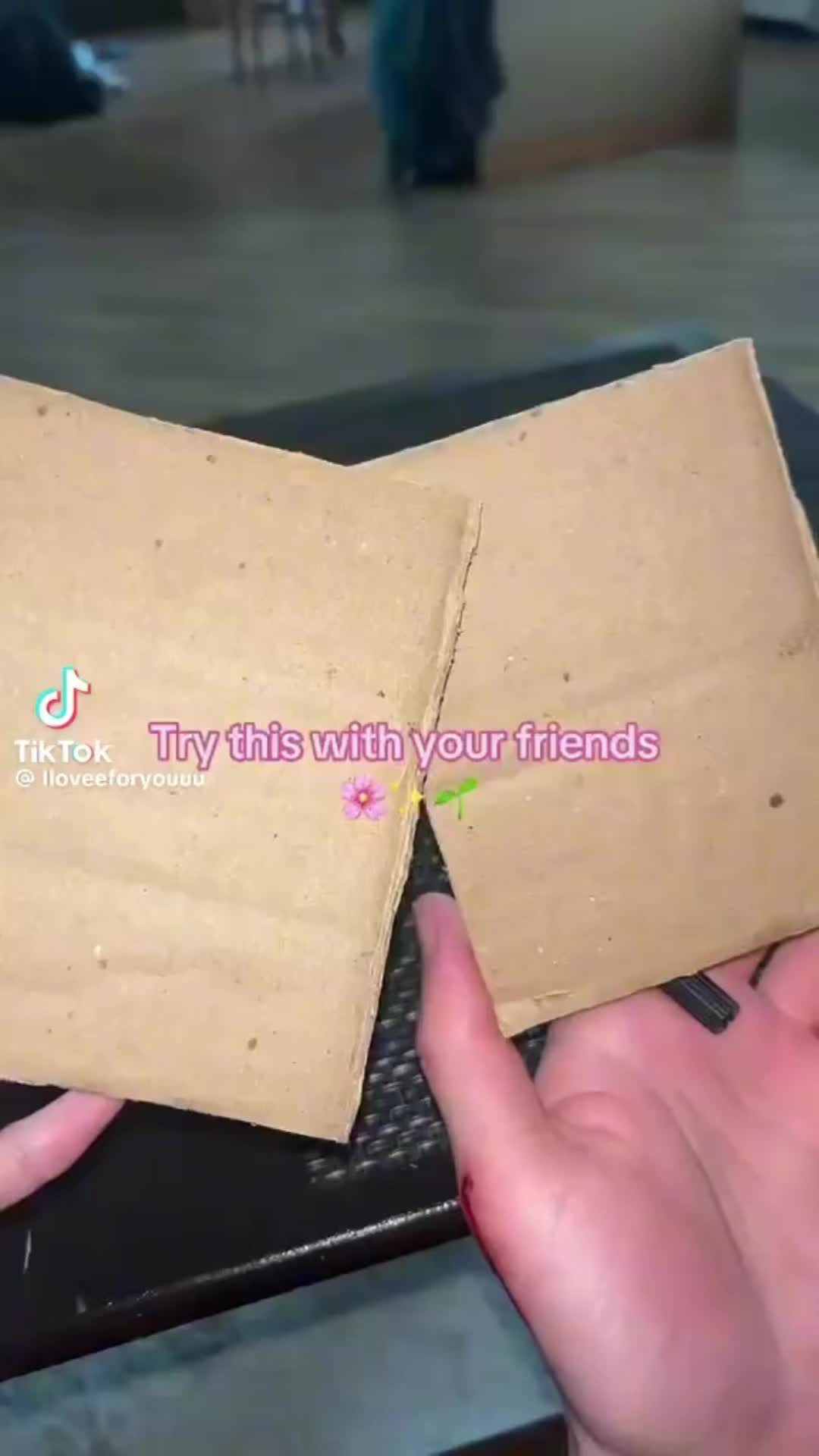 This may contain: someone is holding two pieces of brown paper in their left hand and the other one has pink lettering on it that says try this with your friends