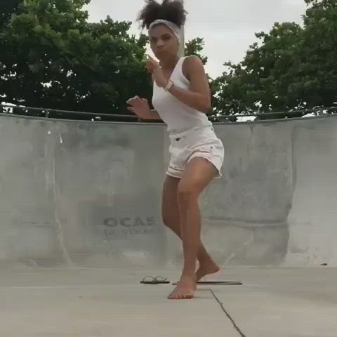 This may contain: a woman in white shirt and shorts playing with a tennis racquet on concrete