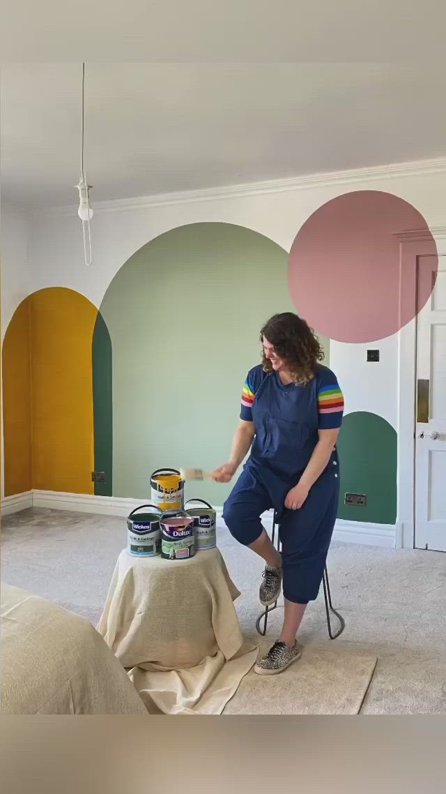 This may contain: a woman in overalls painting a room with circles on the wall and flooring