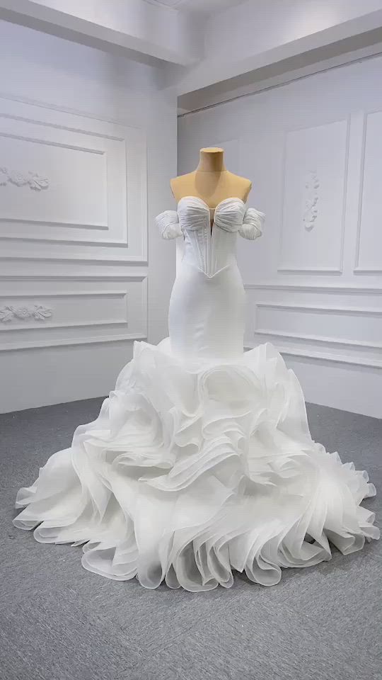 This may contain: a white wedding dress with ruffled layers on display in a studio space, showing the bustle and back of the gown