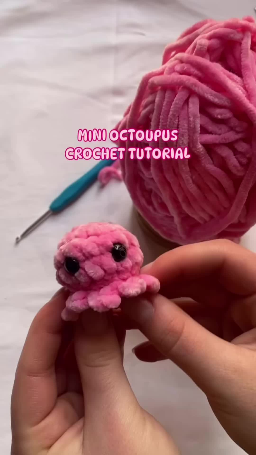 This may contain: a hand holding a pink ball of yarn and a crochet octopus