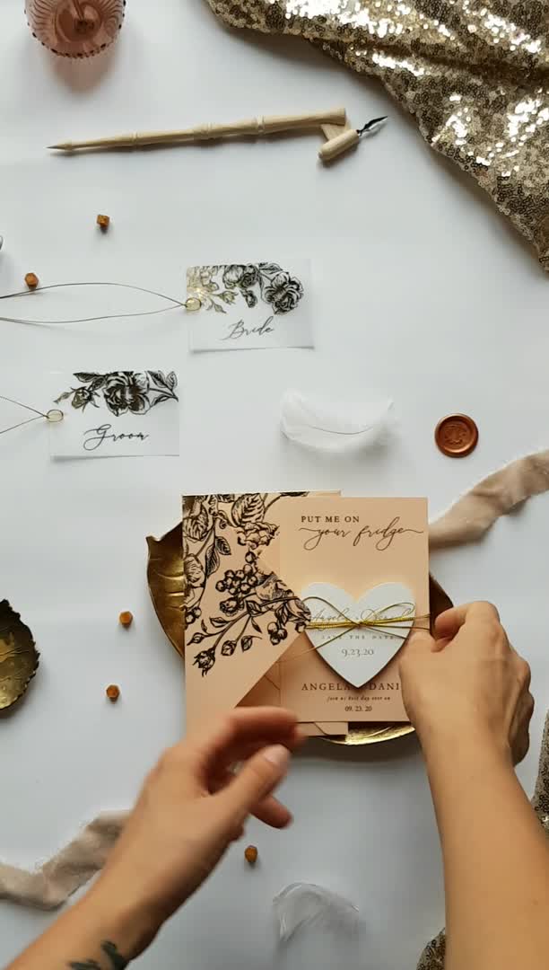 This may contain: two hands holding envelopes with the words save the date magnet heart on them and gold foil