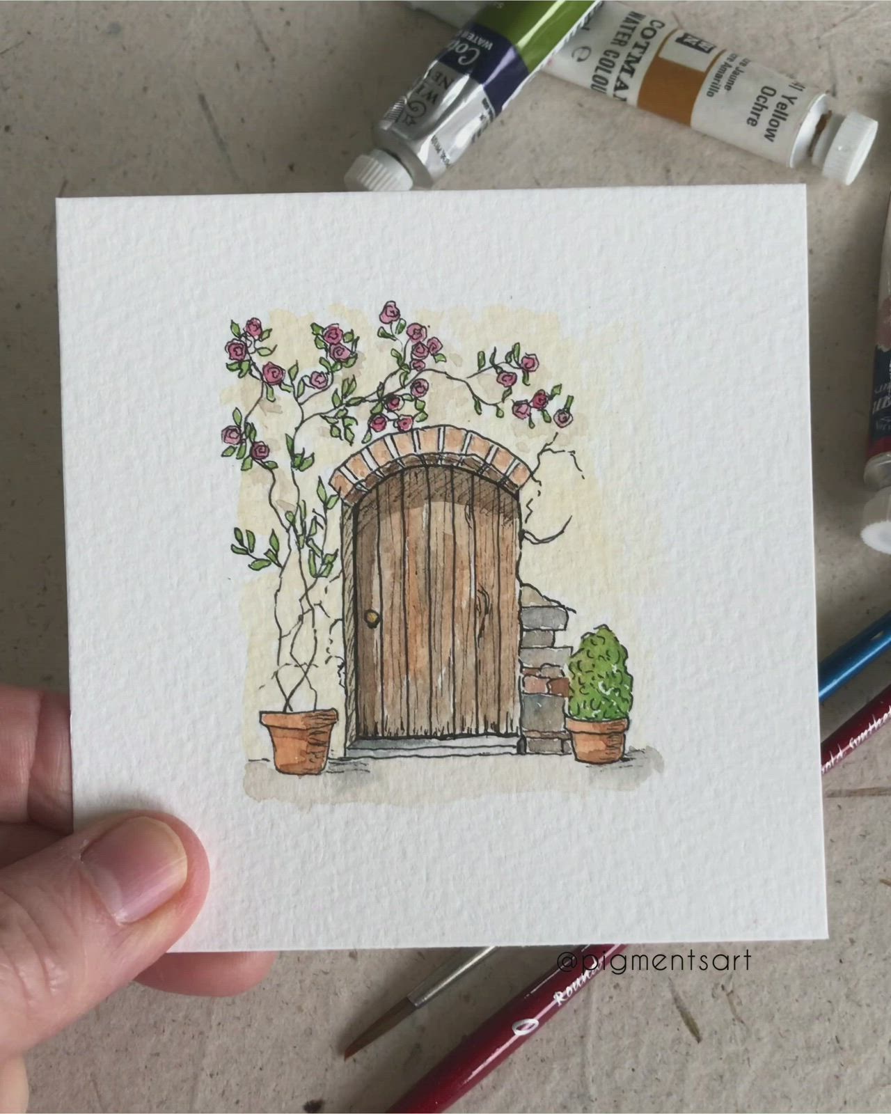 This may contain: a hand holding up a card with an image of a door and potted plants