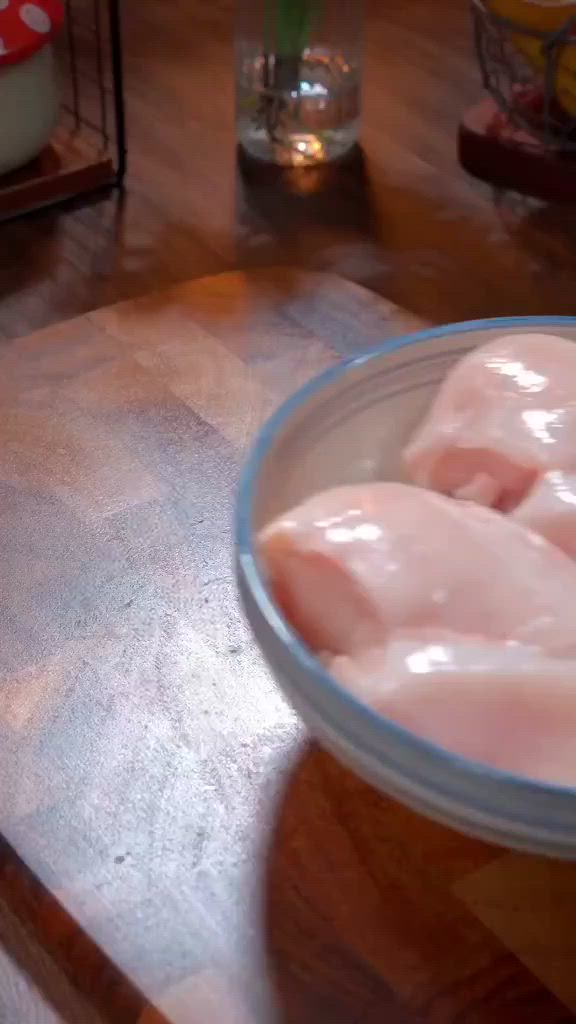 This may contain: two pieces of raw chicken in a bowl on a wooden counter top next to other food items