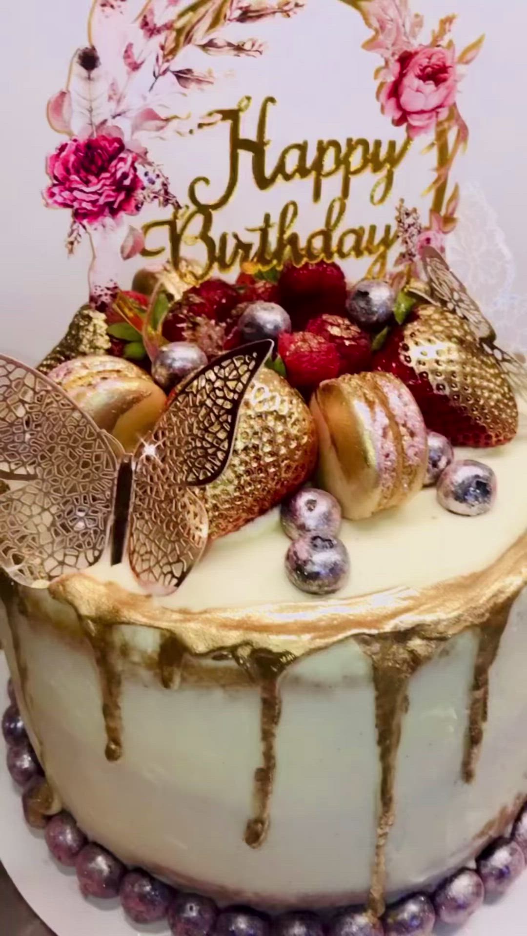 This may contain: a birthday cake with strawberries and berries on top, is decorated with gold icing