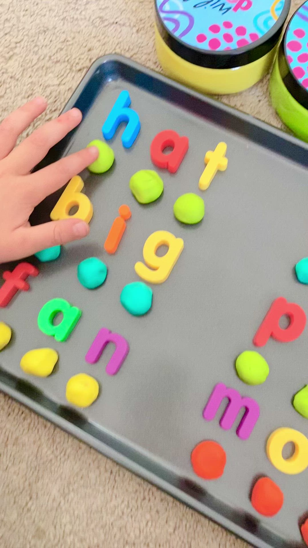 This may contain: a child's hand is touching the letters on a tray with plastic magnets