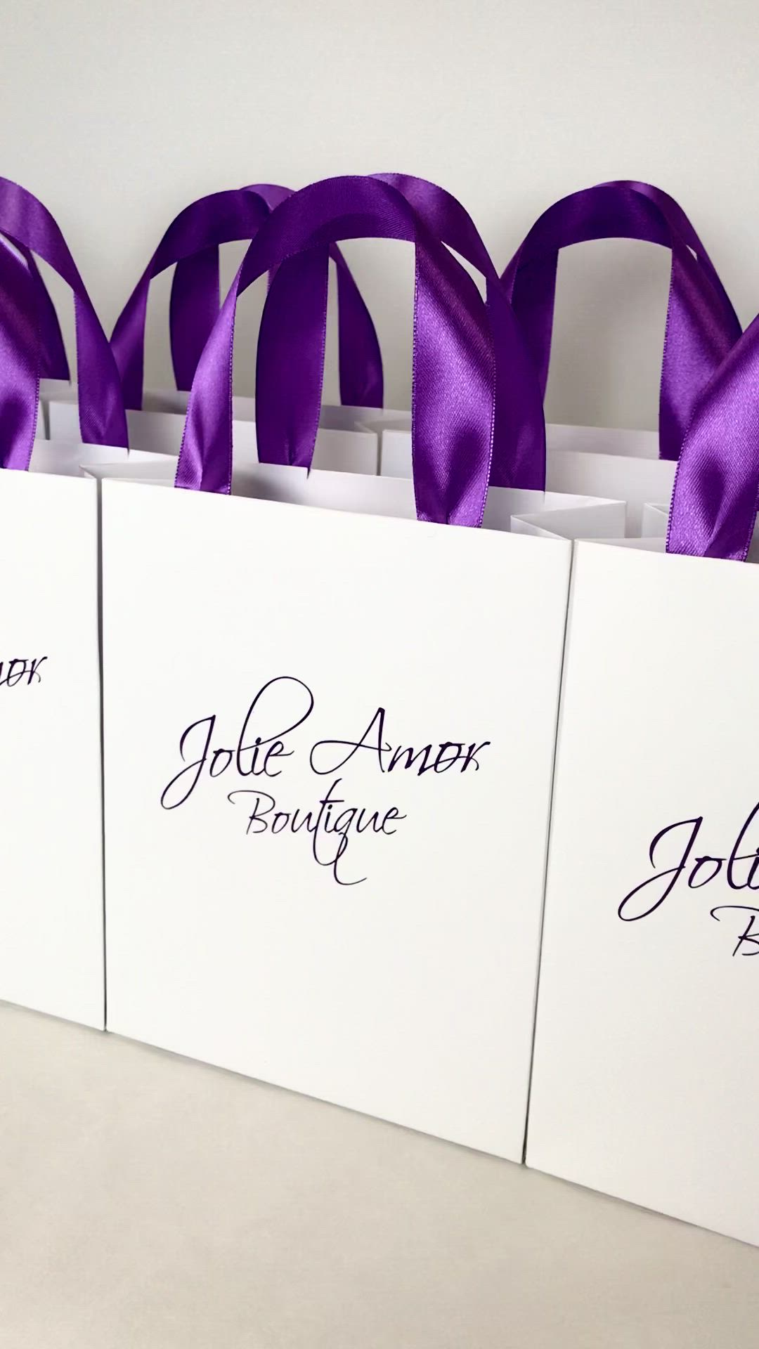 This may contain: four white bags with purple ribbons tied to the front and back of them, each bag has an individual name on it