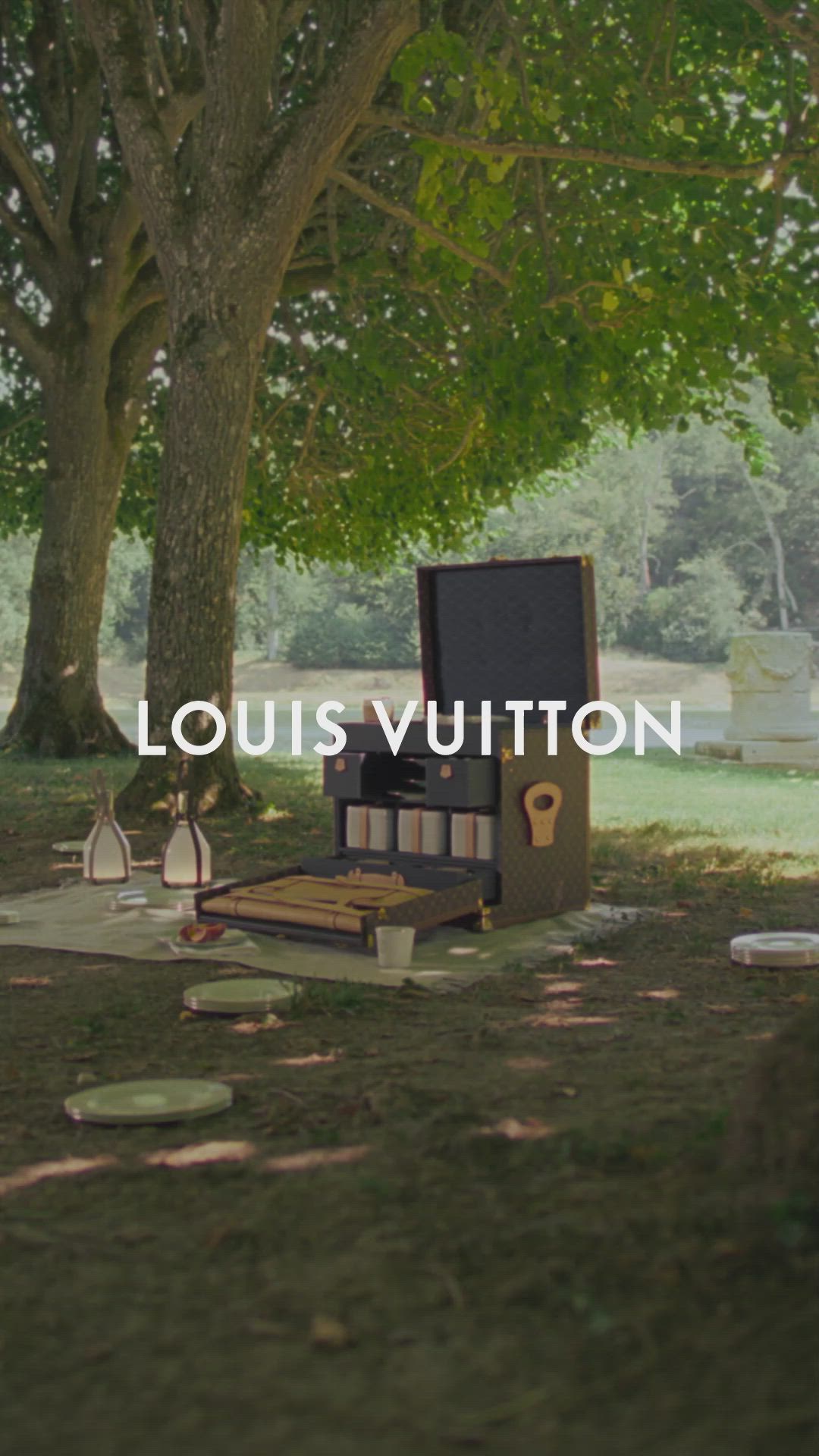 This may contain: an open suitcase sitting on top of a grass covered field next to a tree with the words louis vuitton above it