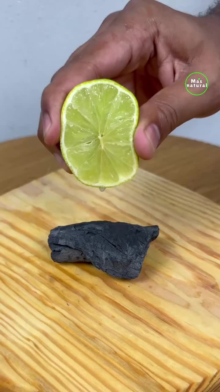 This may contain: a person is holding a lime over a piece of black rock on a wooden table