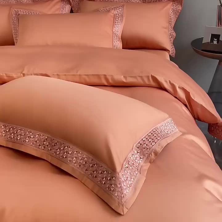 This may contain: a bed with an orange comforter and matching pillow cases, along with a magazine