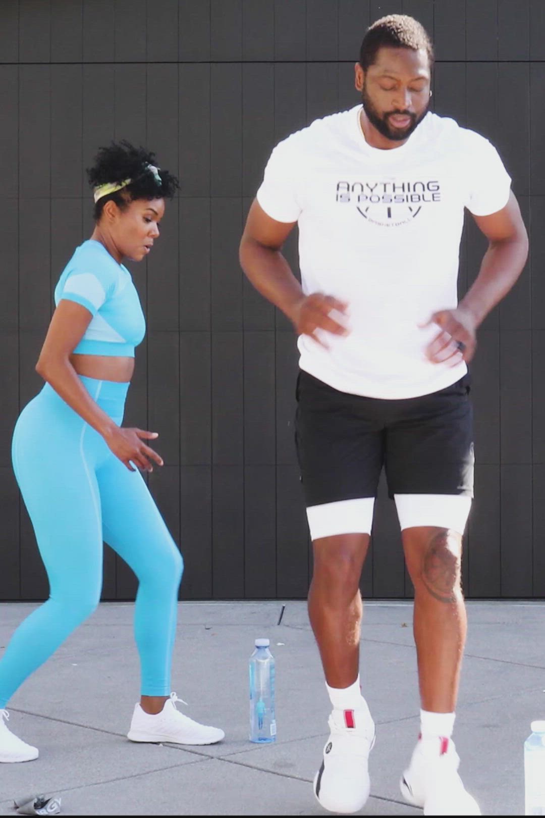 This may contain: a man and woman standing next to each other in front of a wall with water bottles