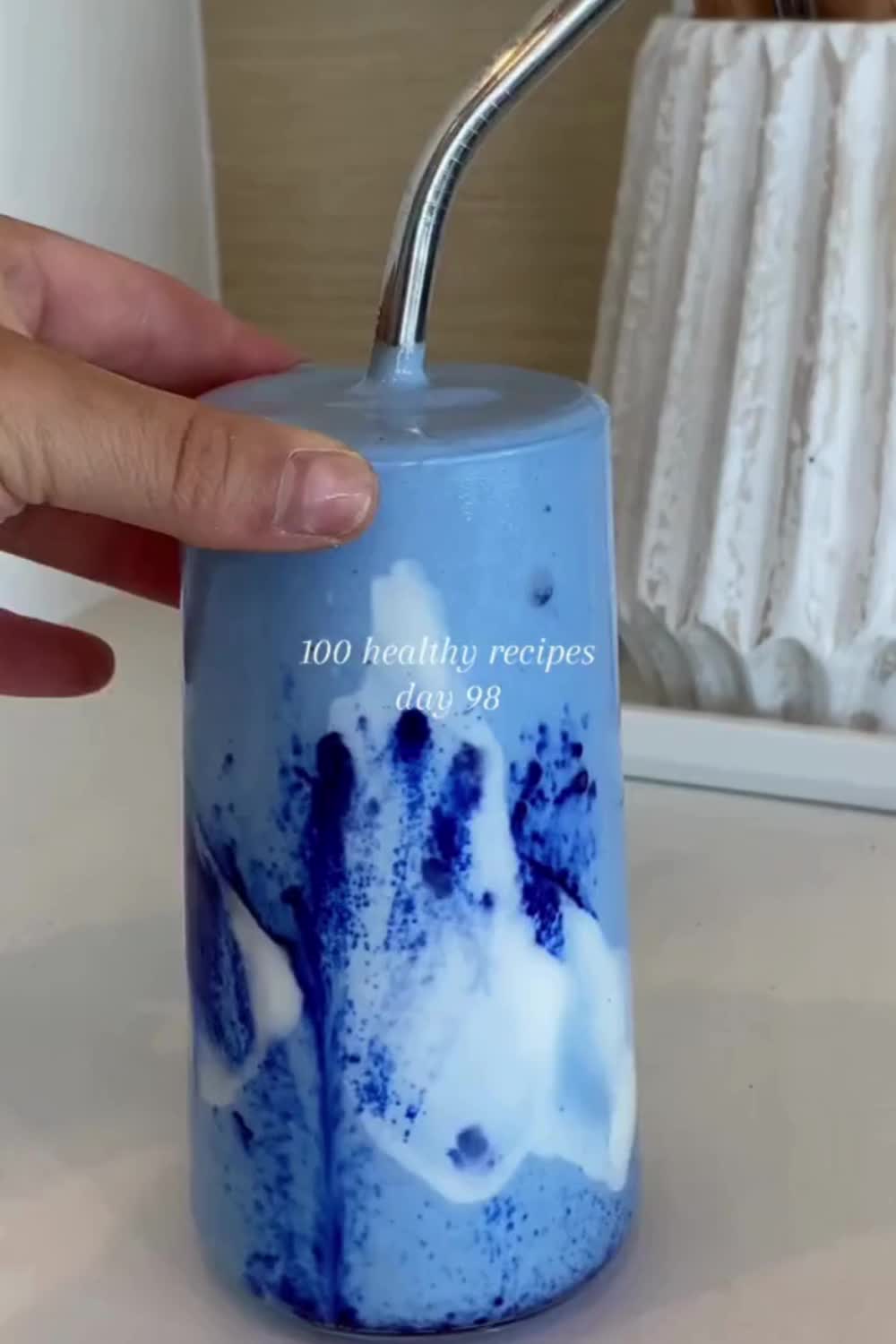 This may contain: a person pouring blue liquid into a glass