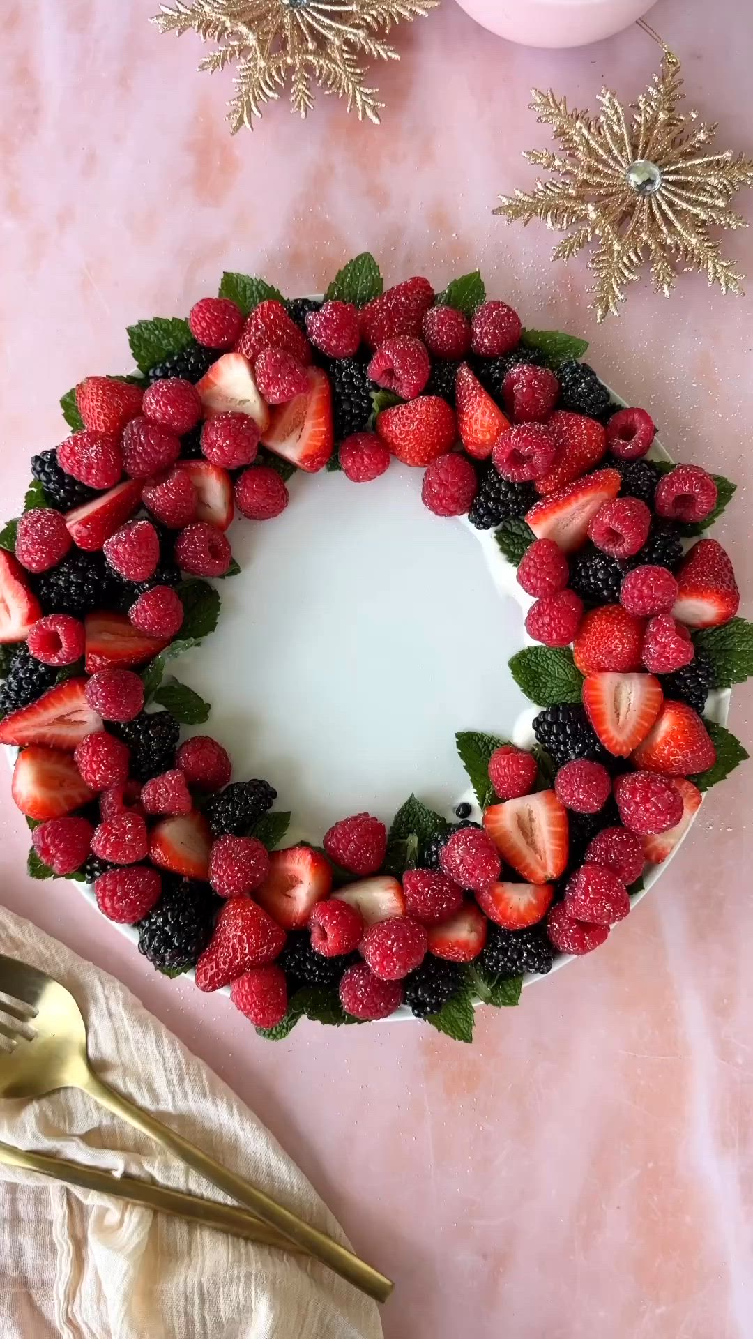 This may contain: a cake decorated with strawberries and leaves on a pink table cloth next to a bowl of berries