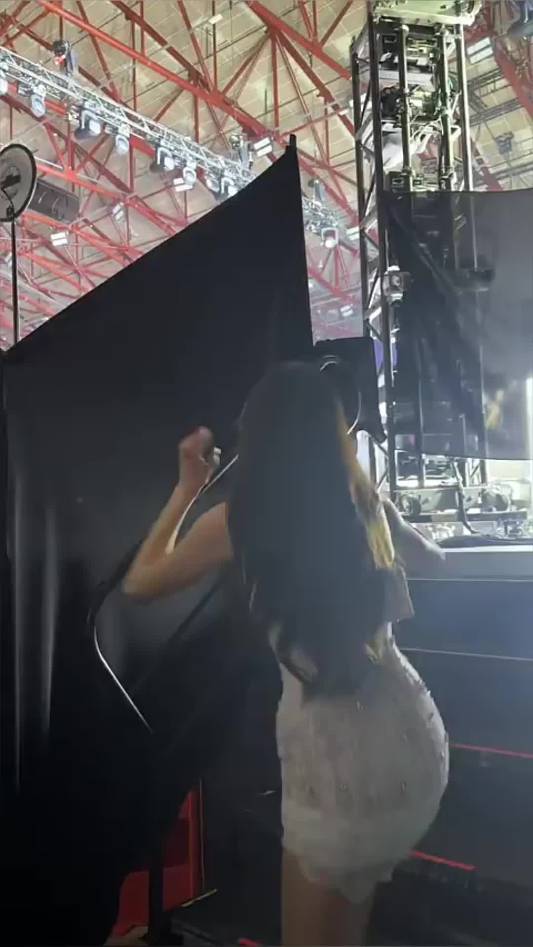 This may contain: a woman in white dress standing on stage with her hand up to the ceiling above her head