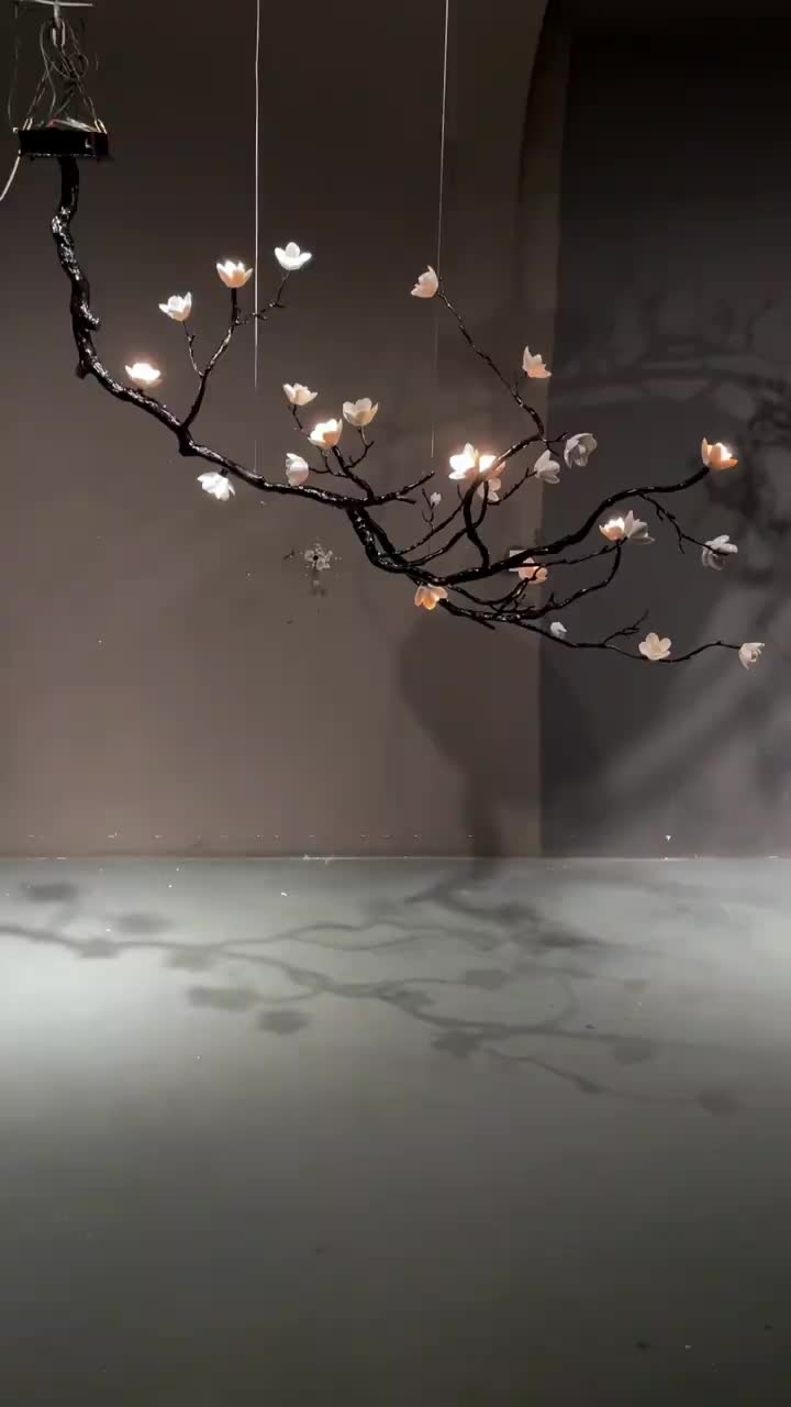 This may contain: a branch with lights hanging from it in front of a gray wall and white floor