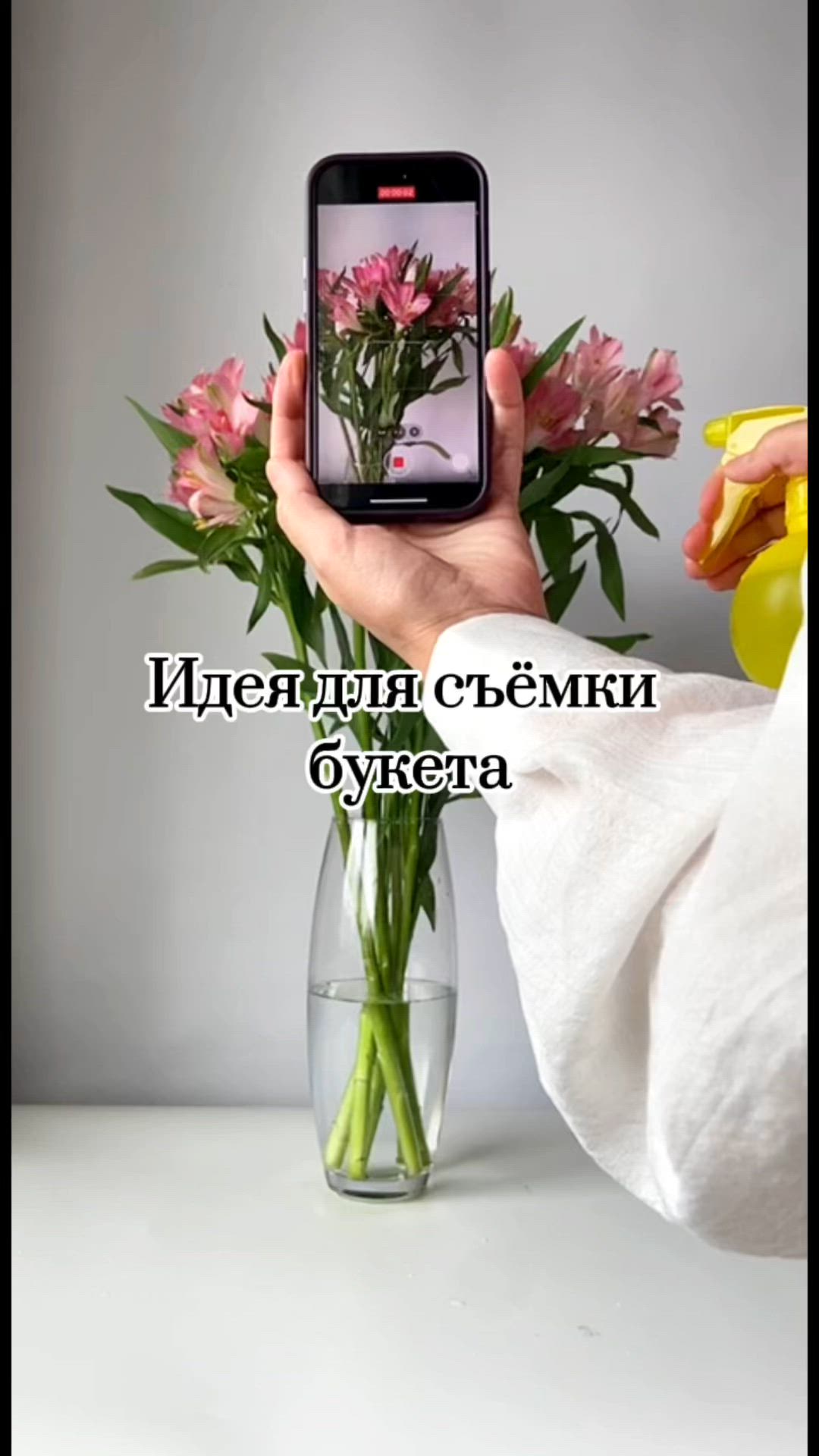 This may contain: a person holding a cell phone in front of a vase with flowers