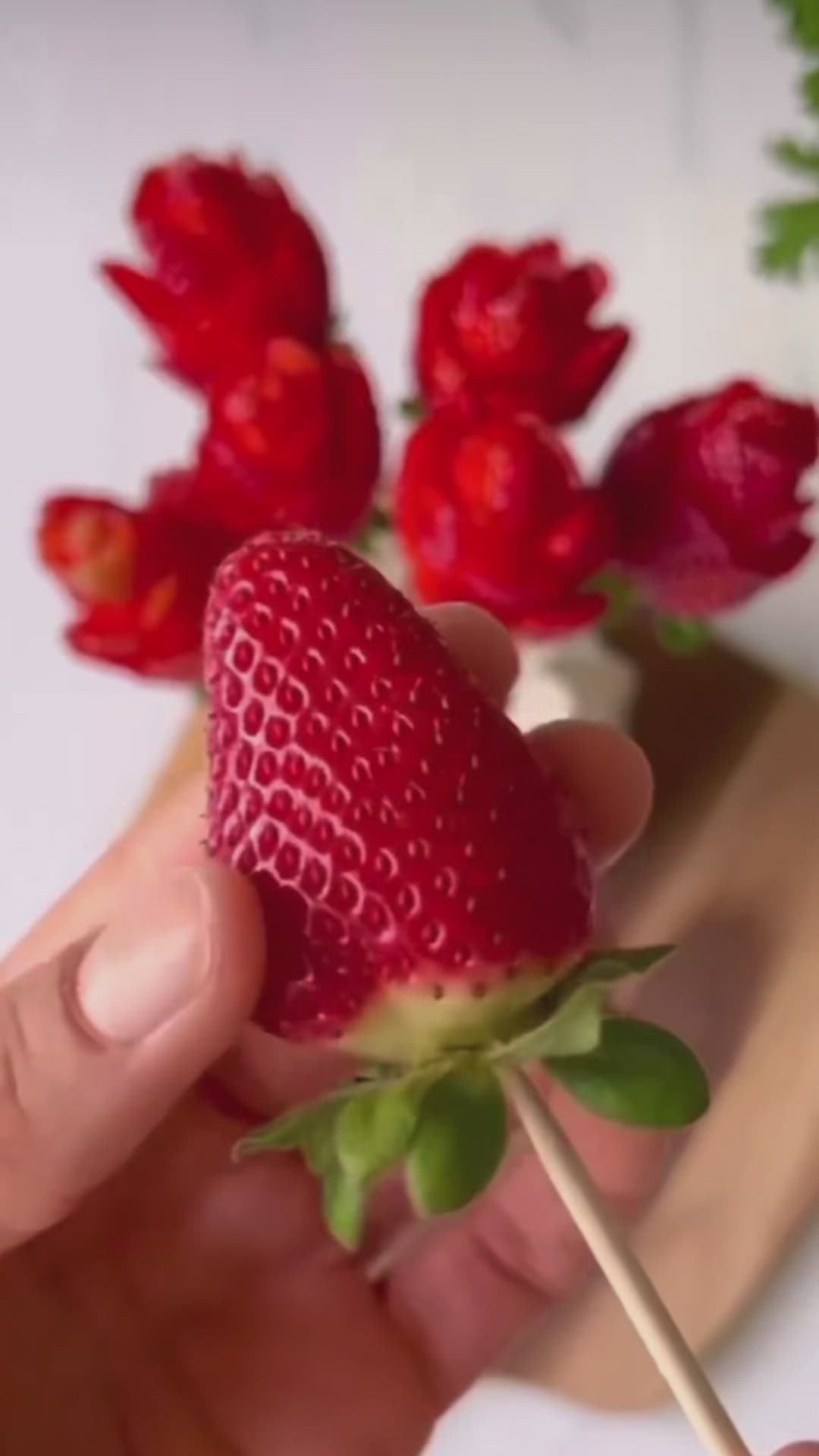 This may contain: a person holding a strawberries on a stick with flowers in the background