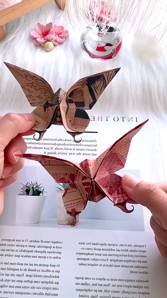 This may contain: two hands holding origami butterflies in front of an open book