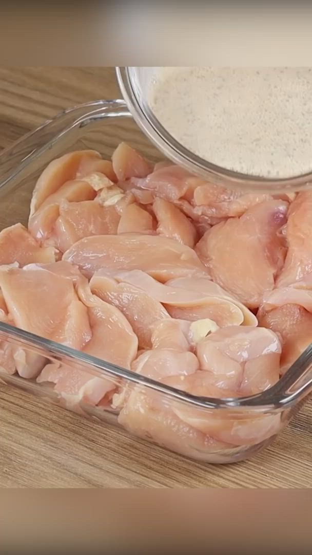 This may contain: chicken being poured into a glass dish on top of a wooden table