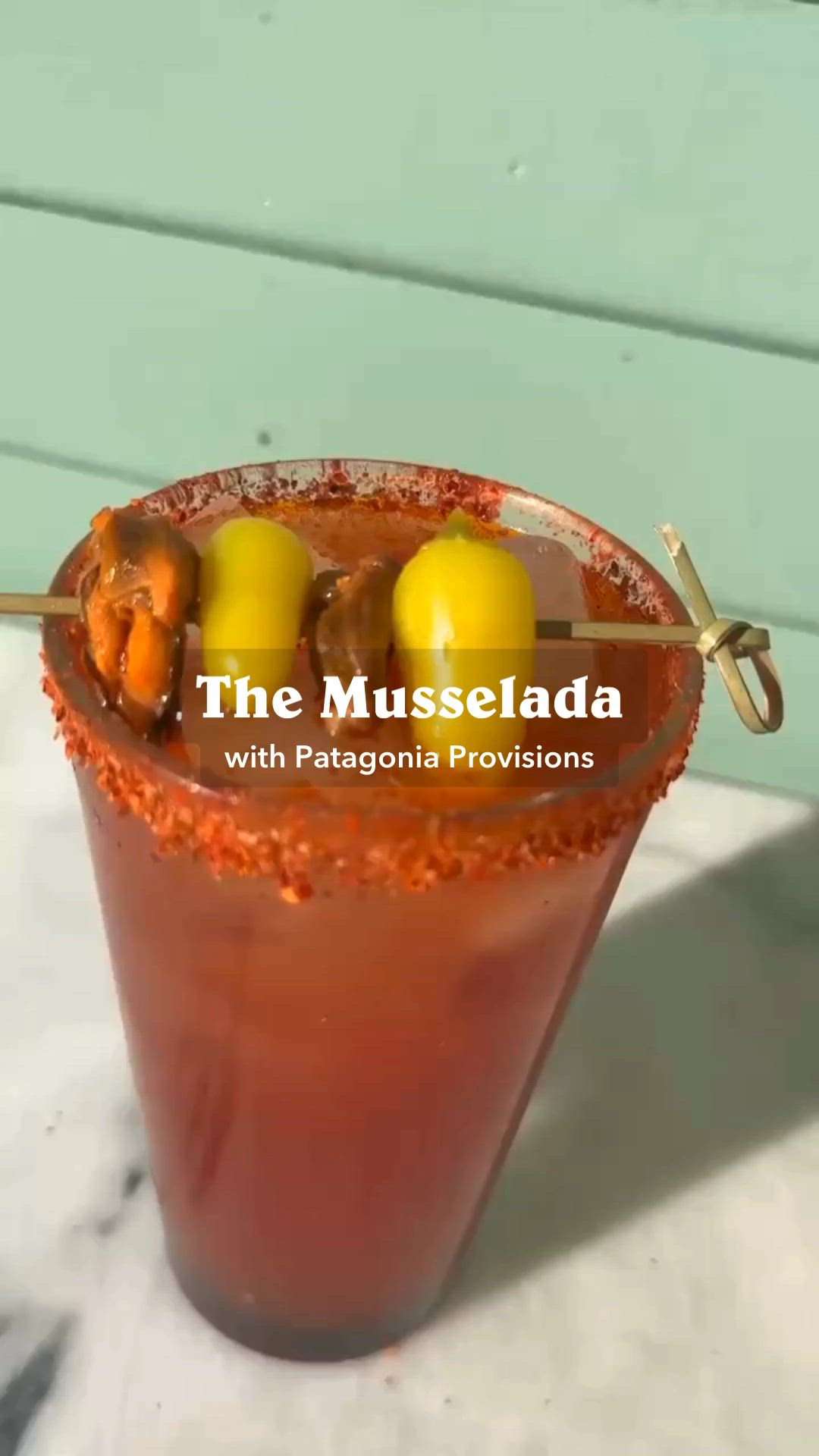 This may contain: the mussellada cocktail is served with hot sauce and chilis in a tall glass