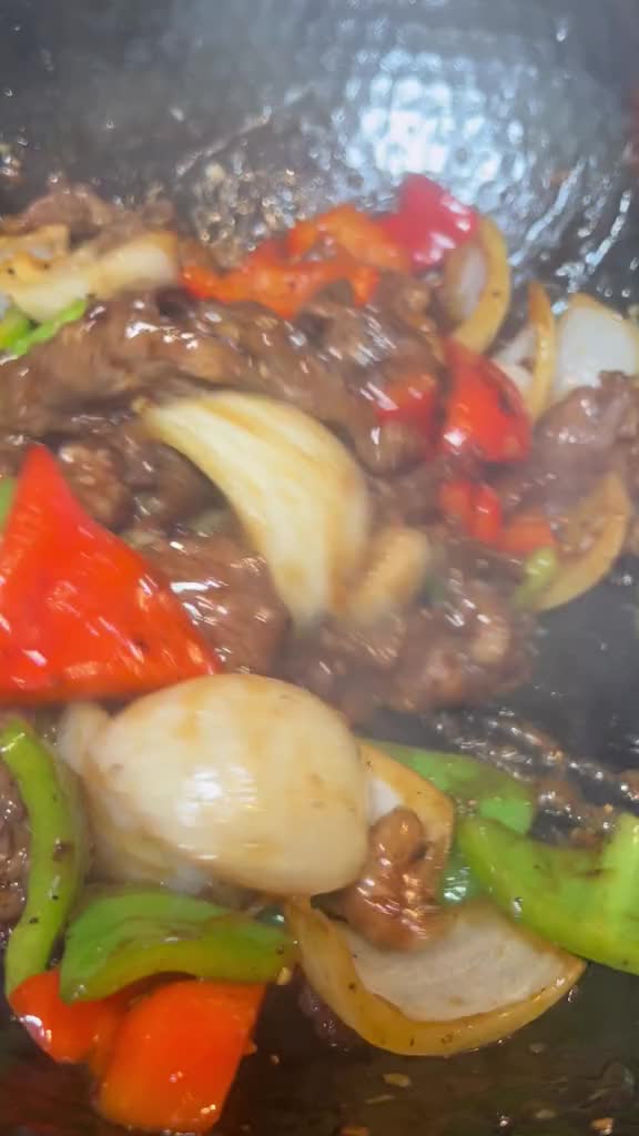 This may contain: stir fry with beef, peppers and onions cooking in a wok on the stove