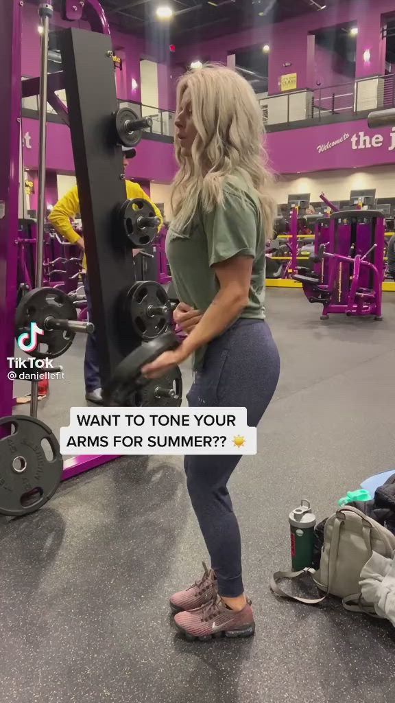 This may contain: a woman is standing in front of a gym machine and looking at the weight rack