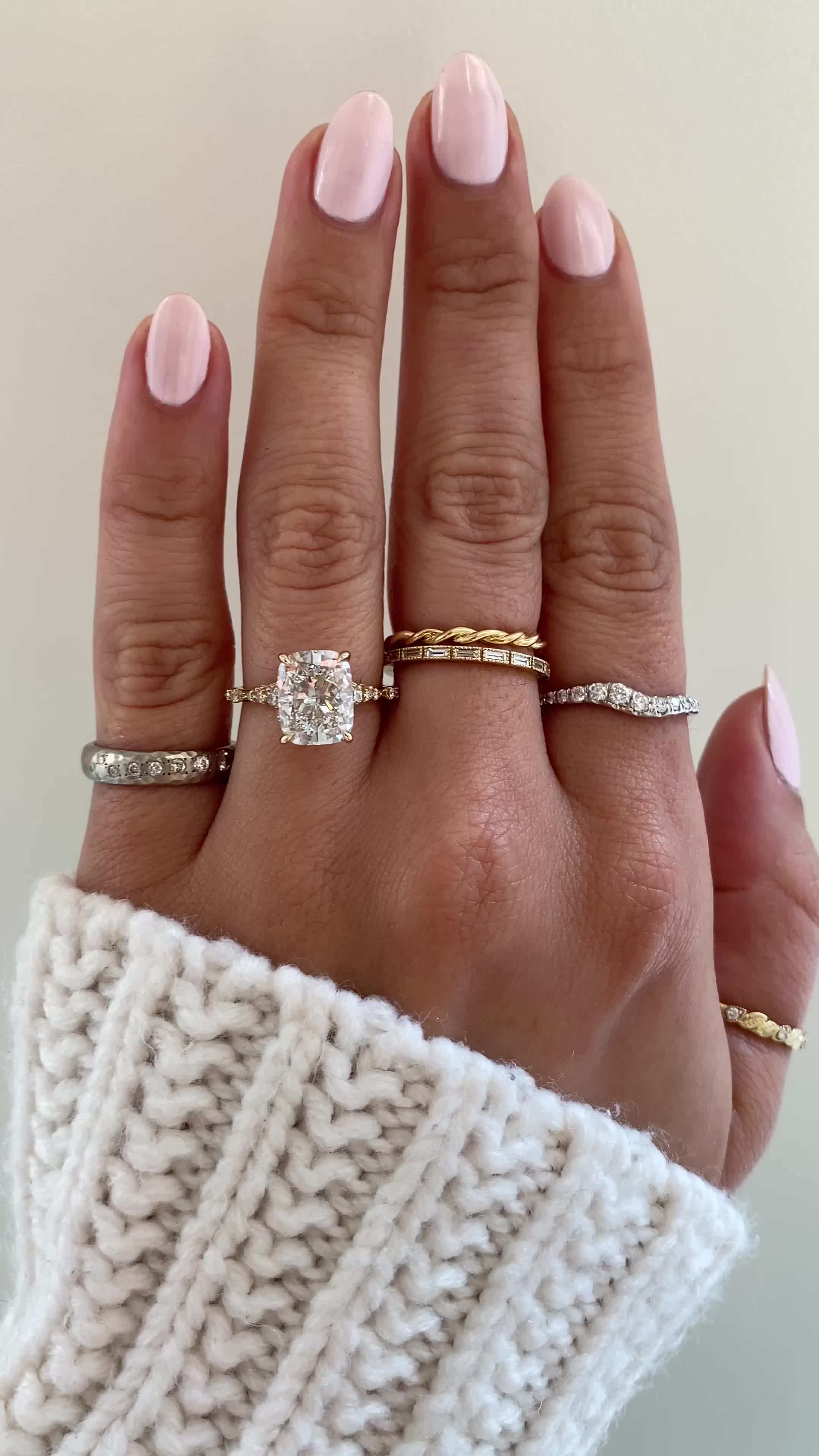 This may contain: a woman's hand with three different rings on her fingers and one is wearing a sweater