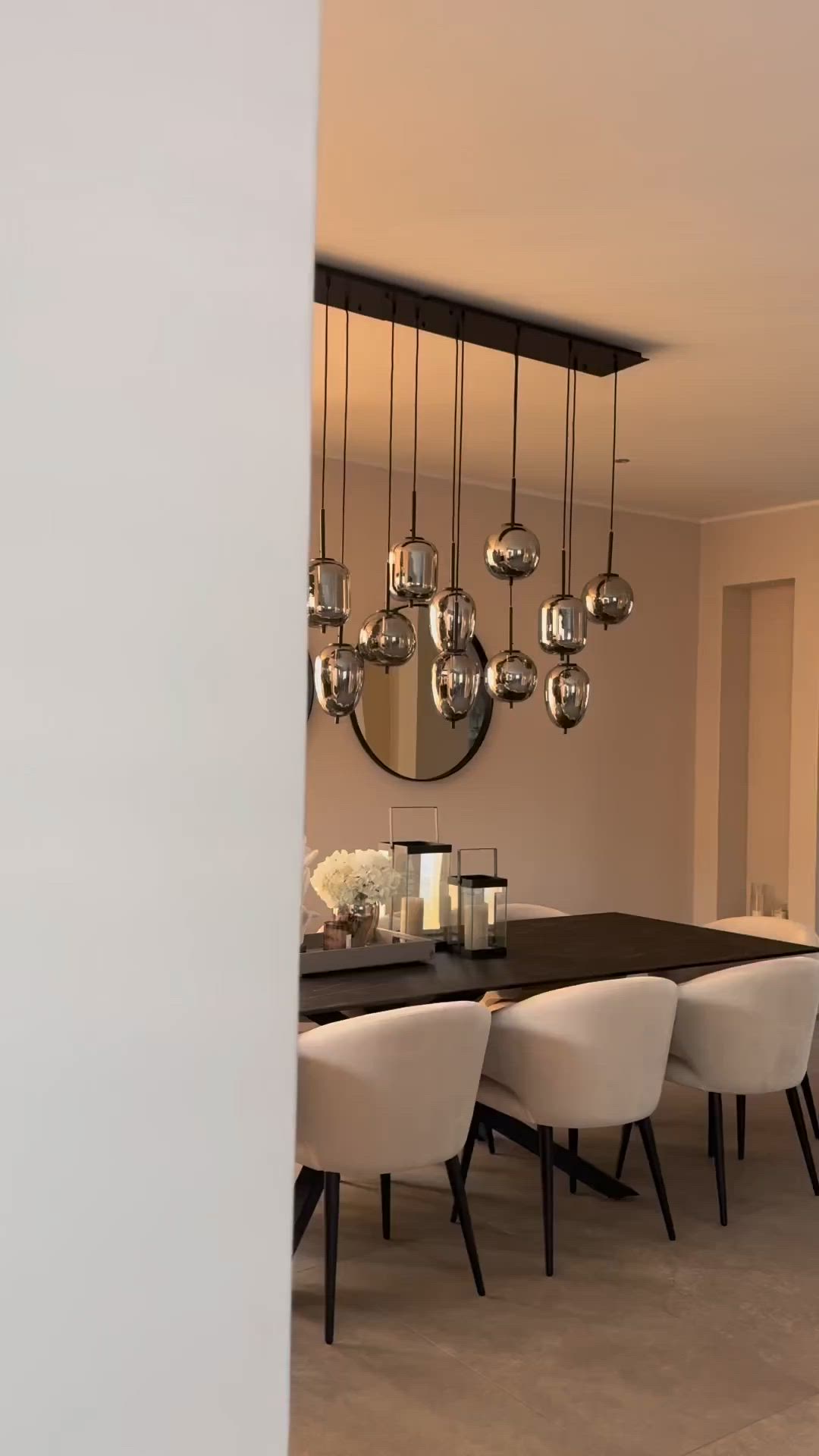 This may contain: a dining room table with white chairs and a large round mirror hanging from the ceiling