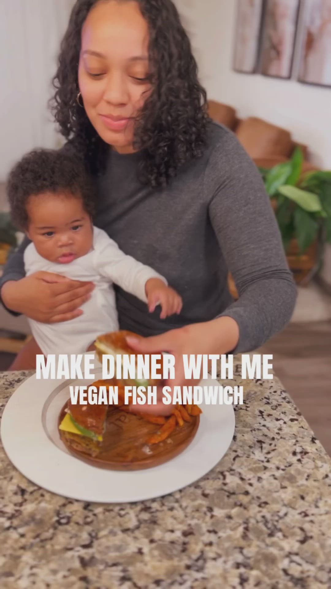 This may contain: a woman holding a baby in front of a plate of food that says make dinner with me vegan fish sandwich