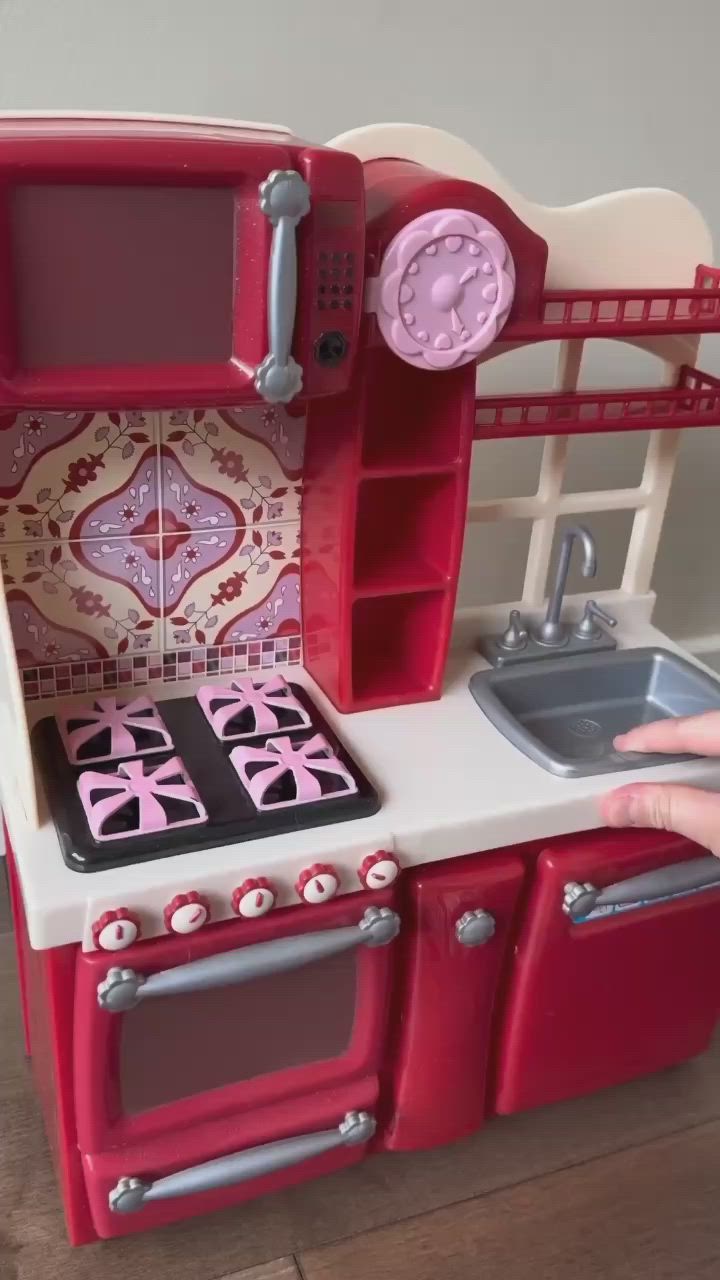 This may contain: a child's play kitchen with red appliances and pink tiles on the counter top