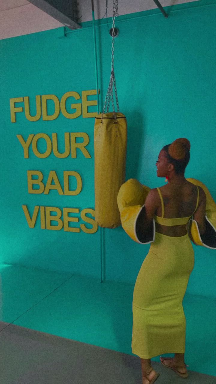 This may contain: a woman wearing a yellow dress and boxing gloves in front of a sign that says fudge your bad vibes