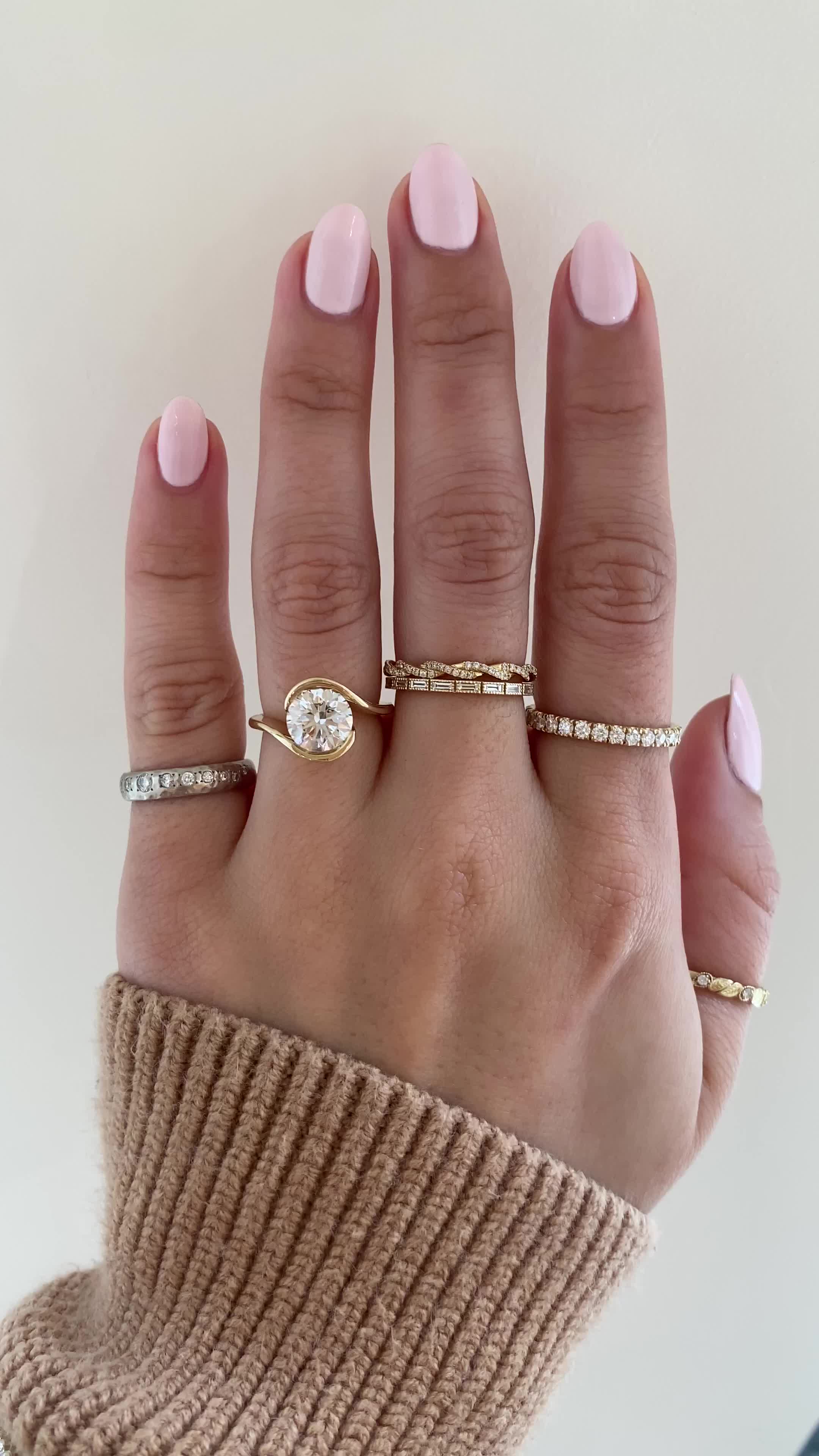 This may contain: a woman's hand with three different rings on her fingers and one is wearing a sweater