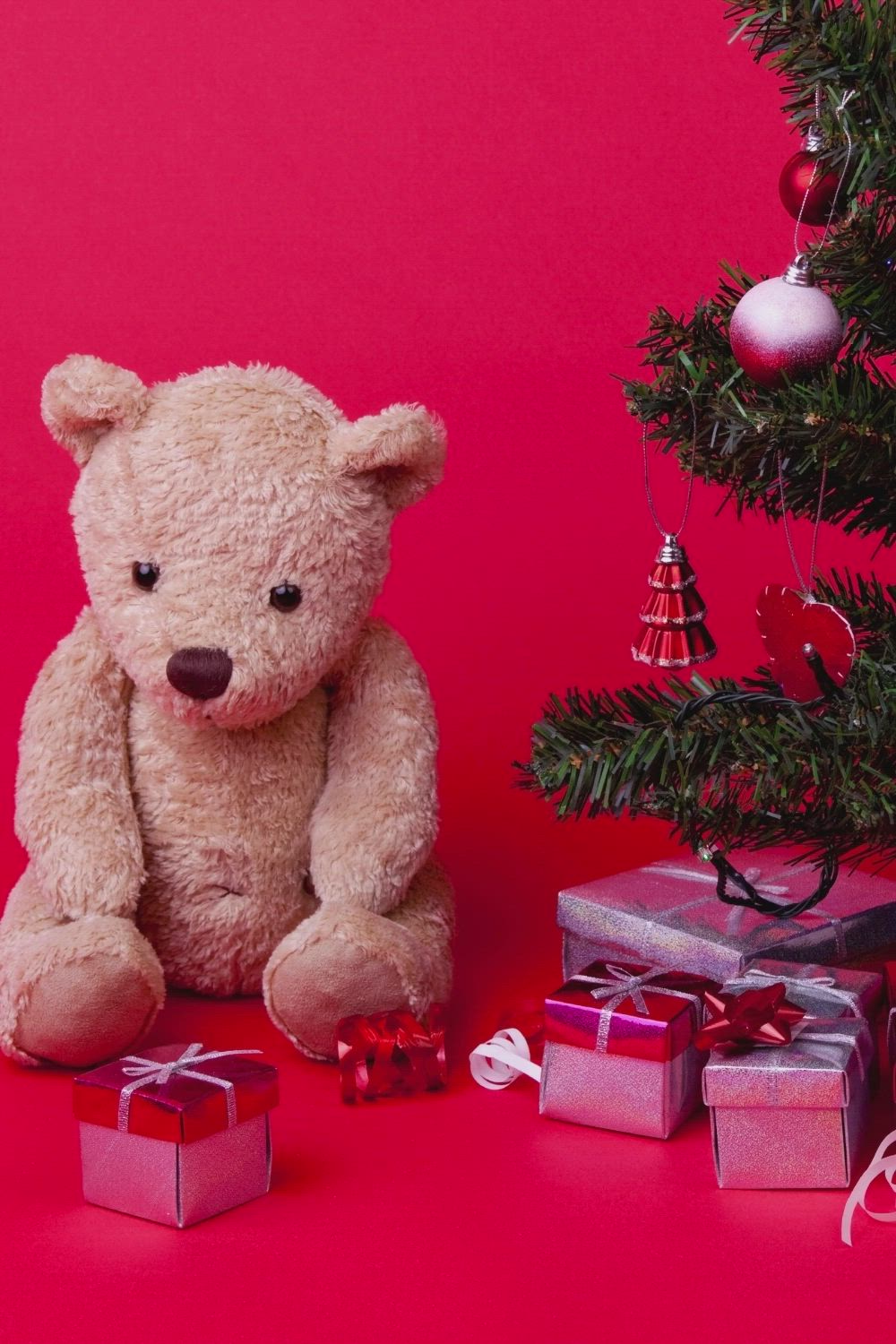 This may contain: a teddy bear sitting next to presents under a christmas tree with the words 20 christmas gifts for your coworkers