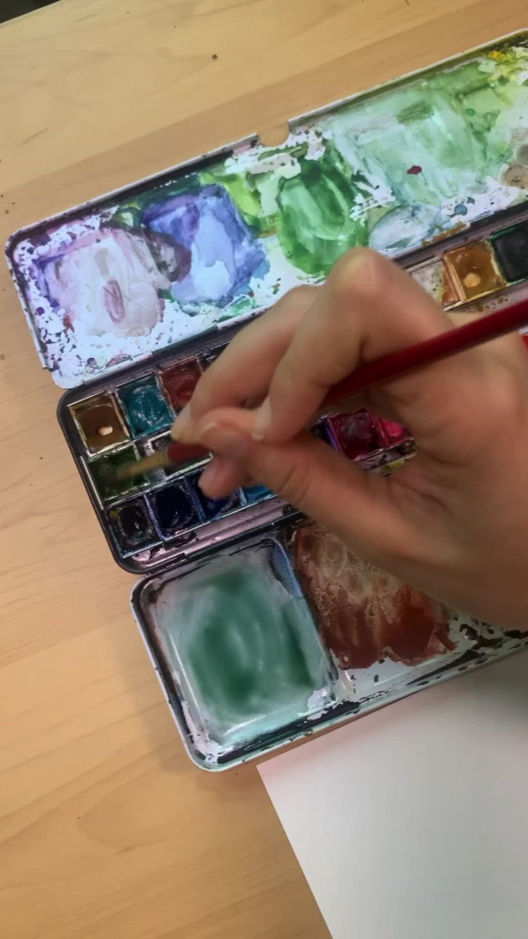 This may contain: someone is painting a christmas tree on paper with watercolors and paintbrushes