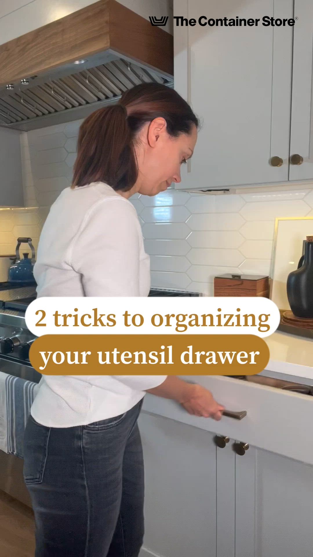 This may contain: a woman standing in front of a kitchen counter with the words 2 tricks to organizing your utensil drawer