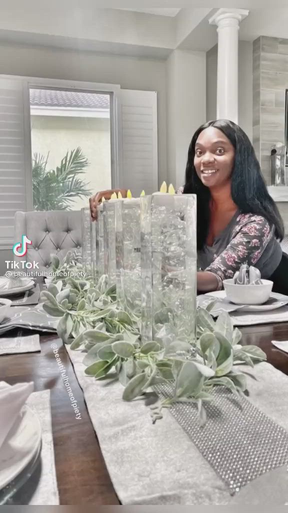 This may contain: a woman sitting at a dining room table in front of a vase with succulents on it