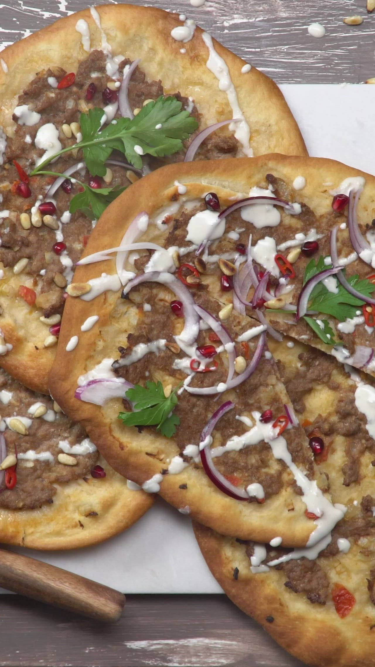 This may contain: three flatbread pizzas with meat, onions and herbs