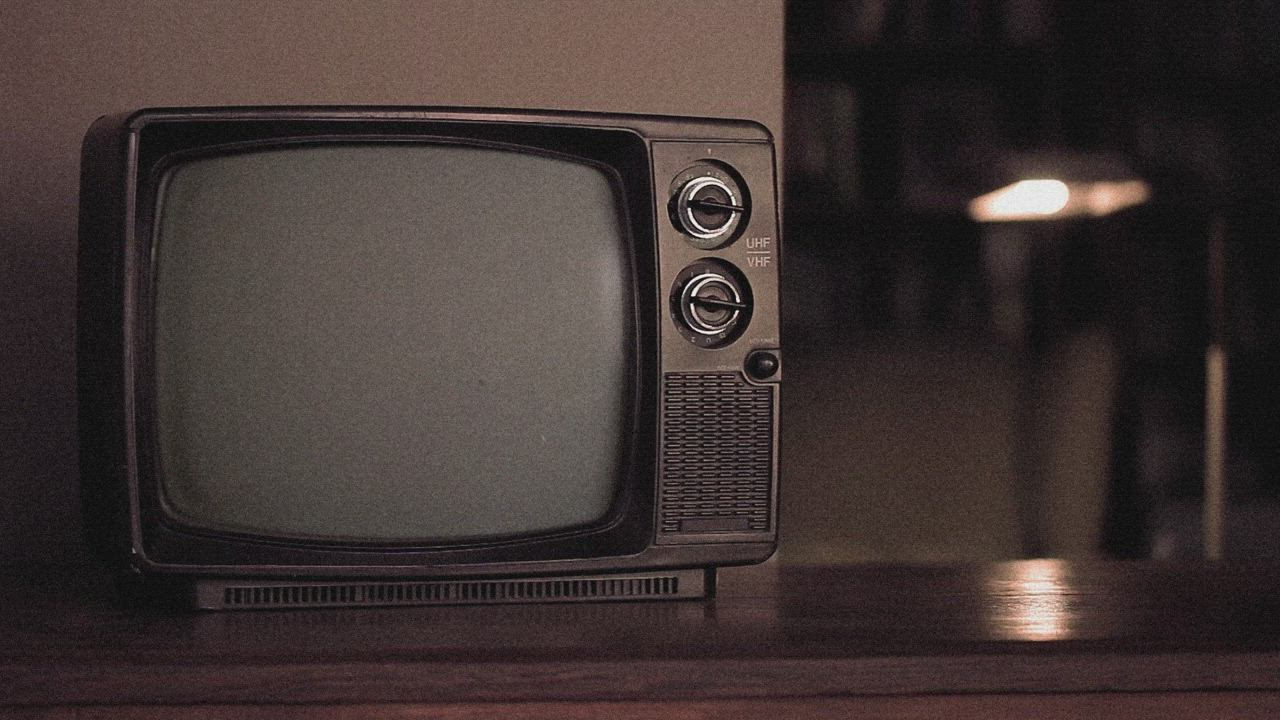 This may contain: an old black television sitting on top of a wooden table in front of a lamp