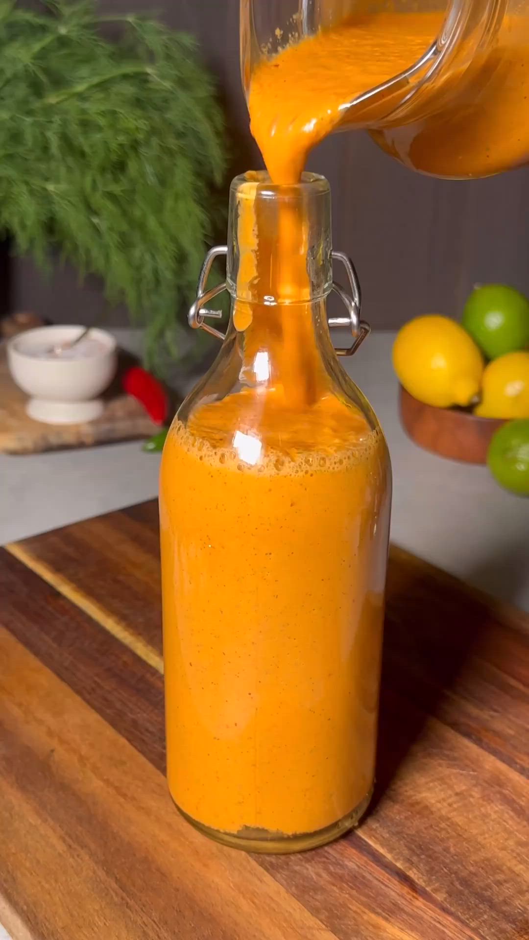 This may contain: a person pouring orange juice into a glass bottle on top of a wooden cutting board