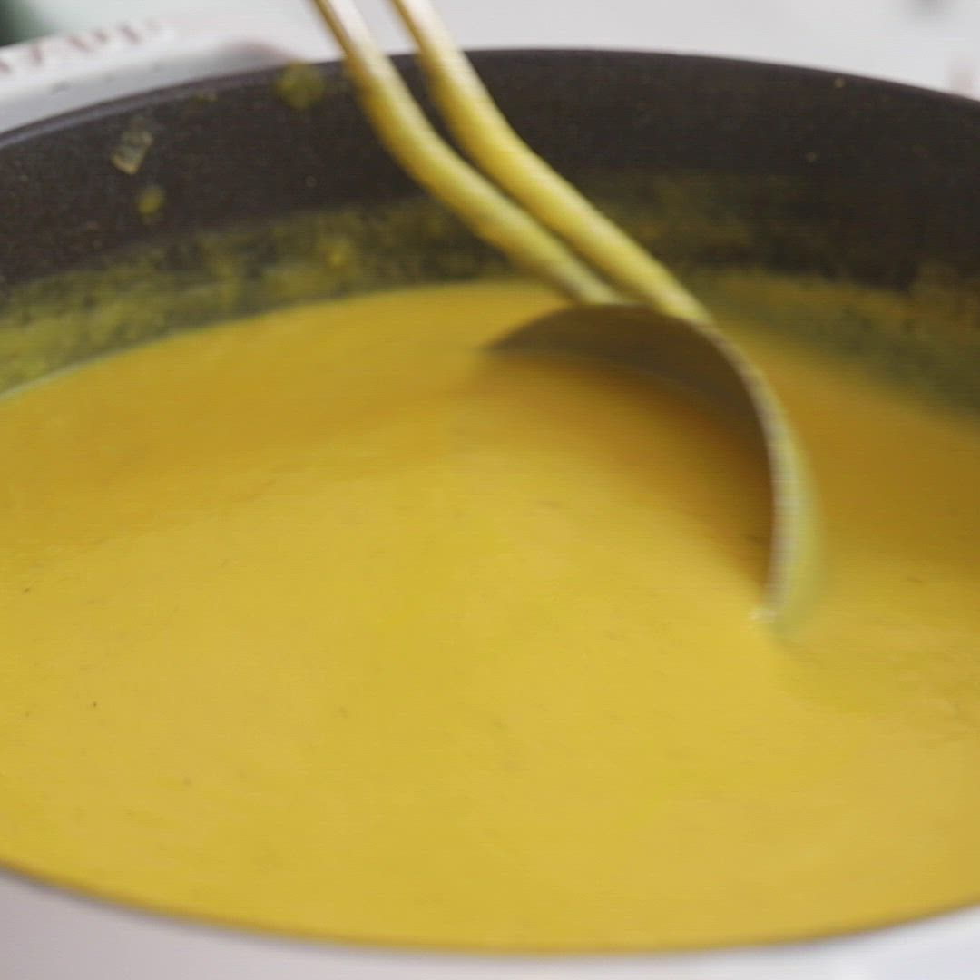 This may contain: a ladle full of yellow liquid being stirred by two wooden spoons