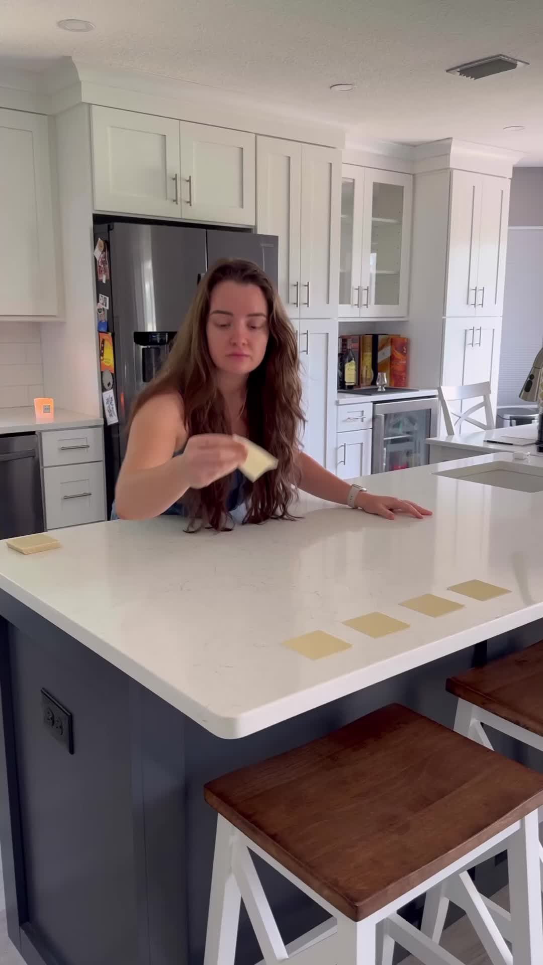 This may contain: a woman standing at a kitchen island with two stools