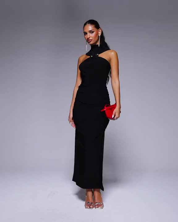 This may contain: a woman wearing a black dress and red clutch bag standing in front of a gray background