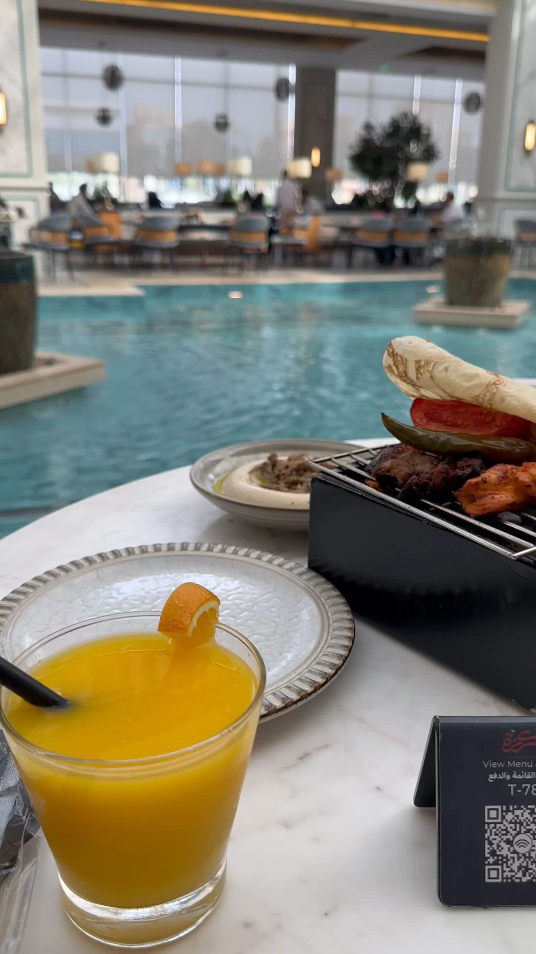 This may contain: a table with food and drinks on it near a swimming pool in a hotel lobby