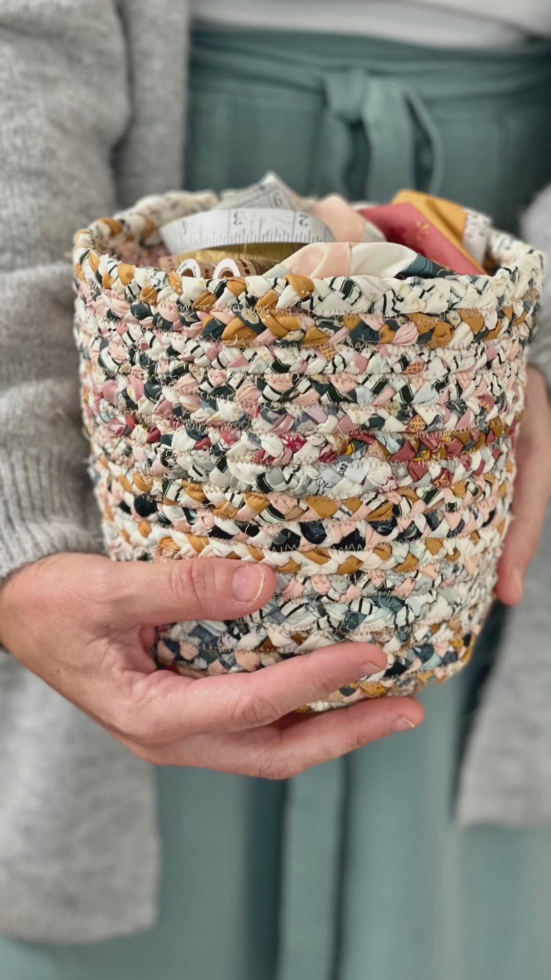 This may contain: a woman is holding a basket full of fabric and sewing needles in her hands while wearing a gray sweater