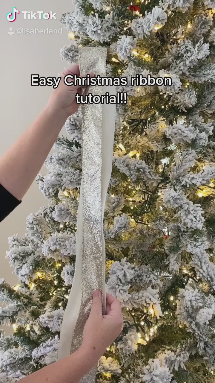 This may contain: someone is holding ribbon in front of a christmas tree with white and silver decorations on it