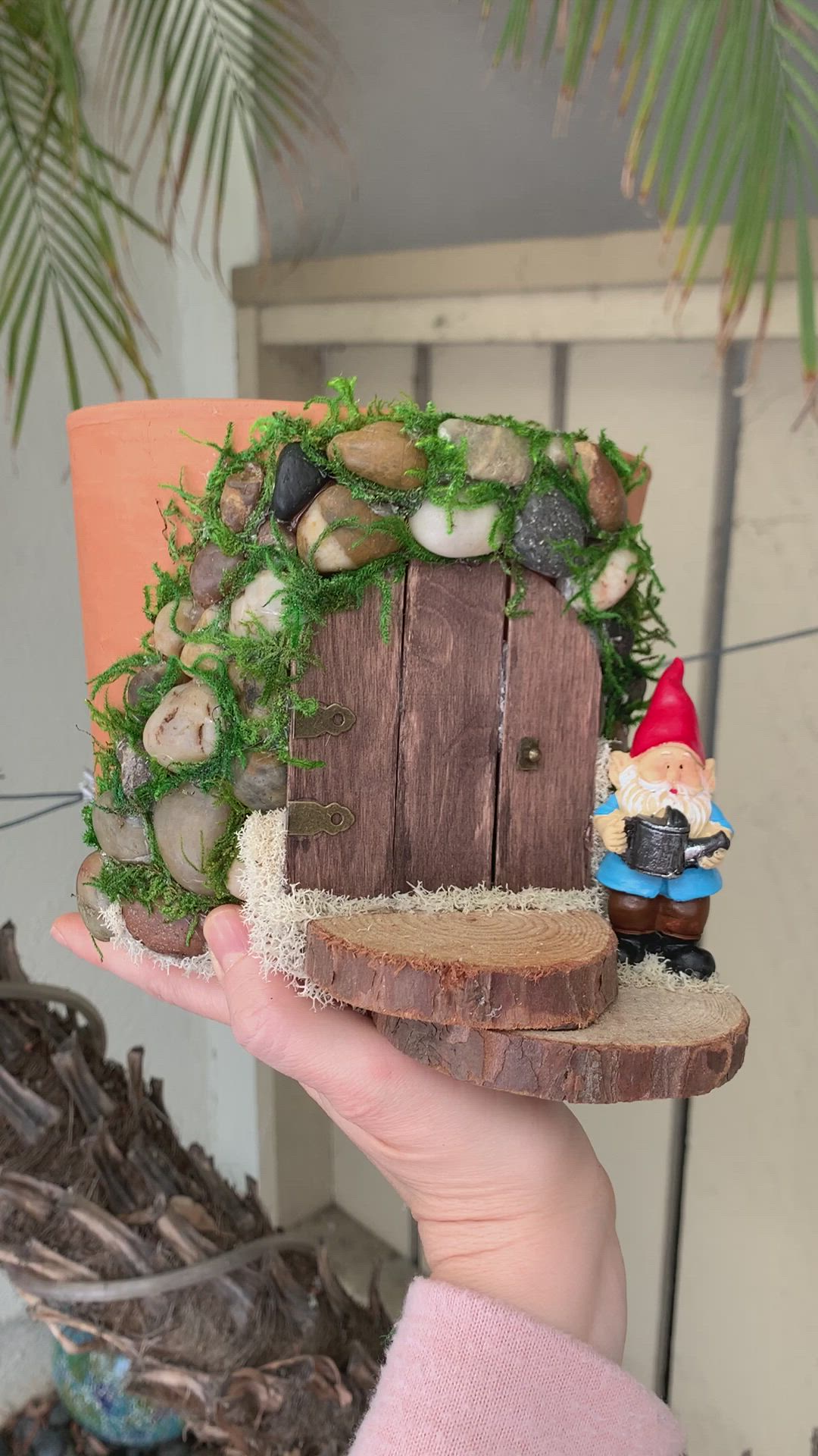 This may contain: someone is holding up a small fairy house made out of wood and moss with a gnome on it