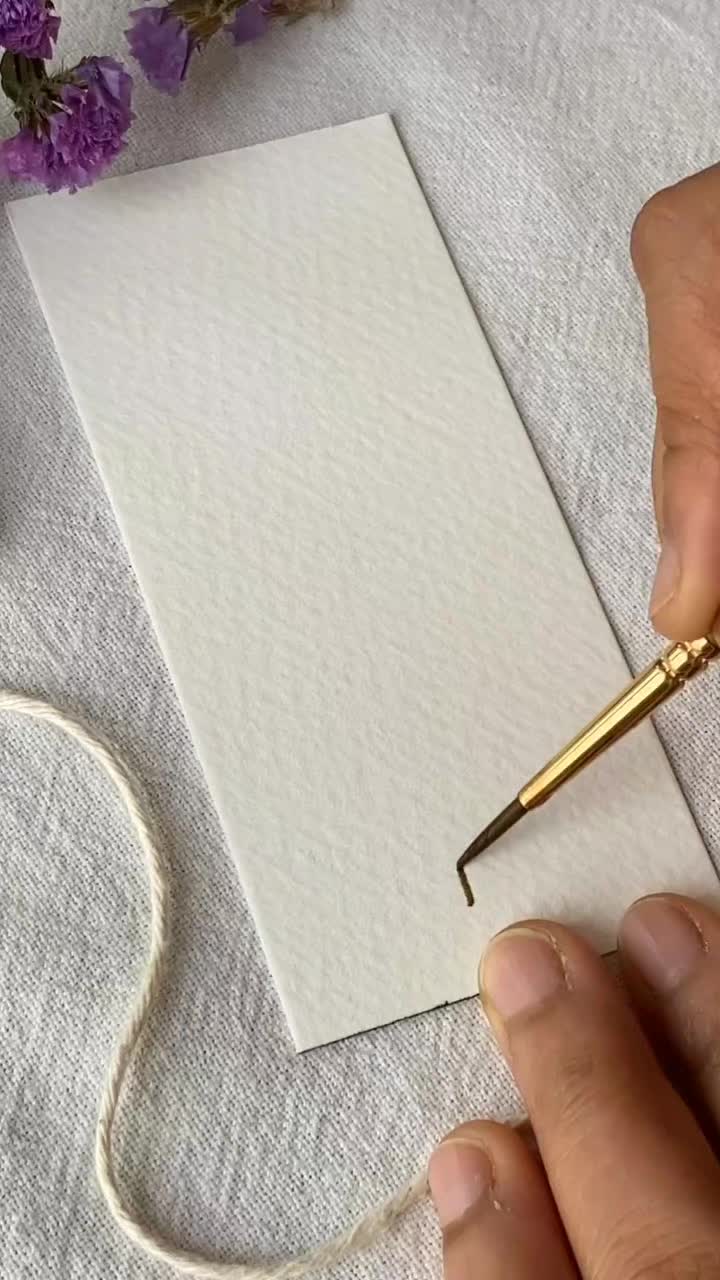 This may contain: a person is painting flowers with watercolors on white paper and gold colored brush