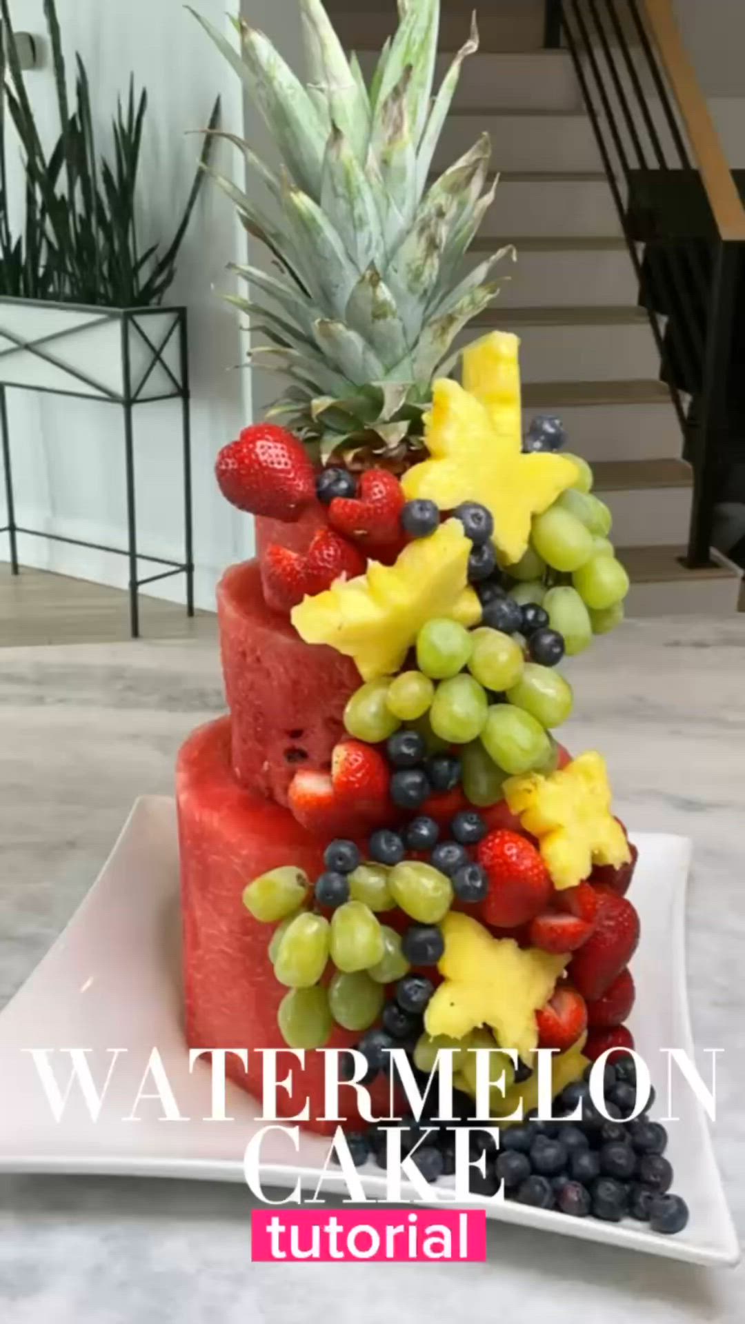 This may contain: a pineapple and watermelon cake with fruit on top is displayed in front of stairs