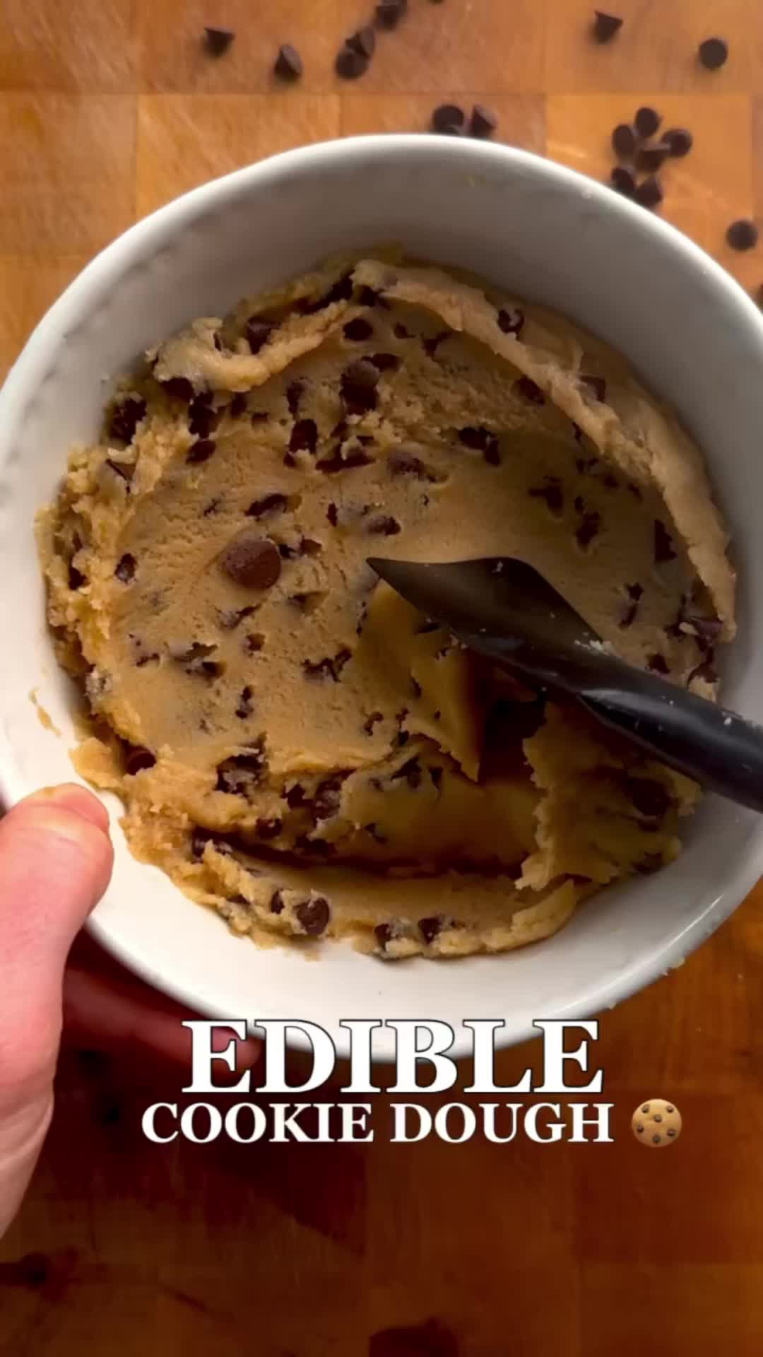 This may contain: a person holding a spoon in a bowl of cookie dough with chocolate chips on the side